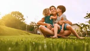 Una persona abbraccia due bambini seduta su un prato al tramonto