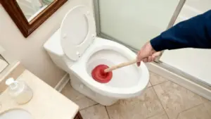 Una persona usa uno sturalavandini rosso per sturare un WC in un bagno domestico