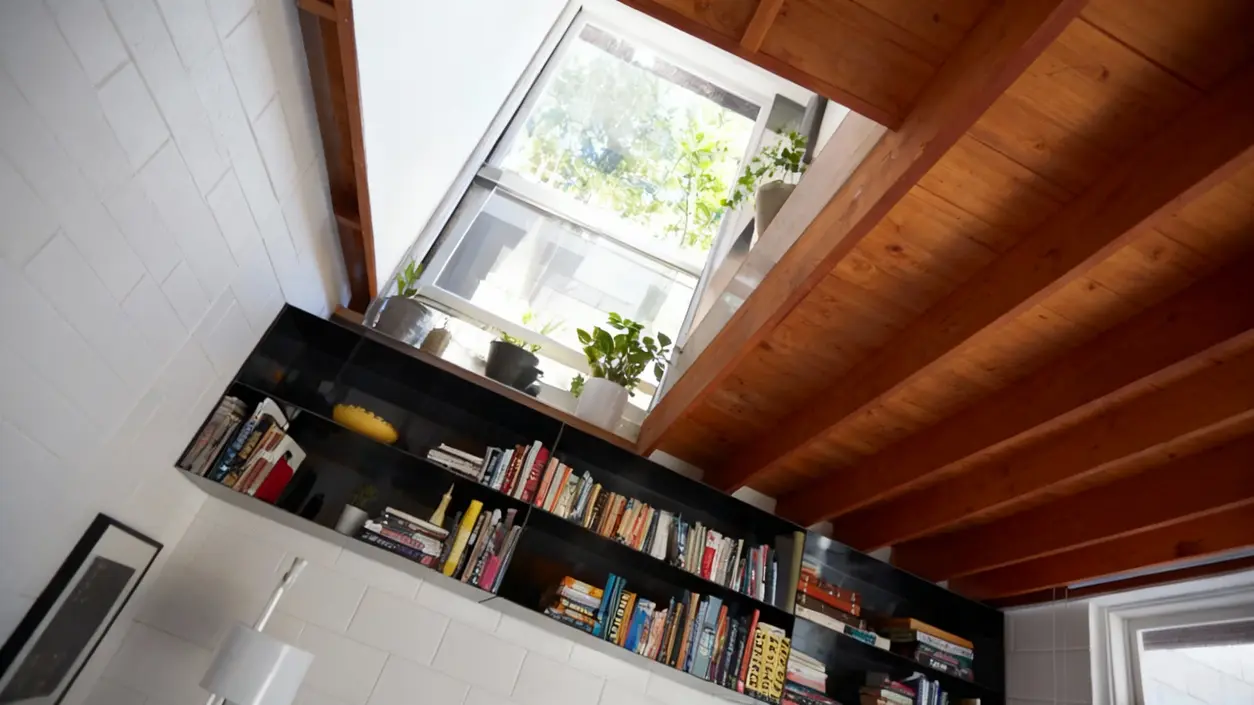Scaffale da salotto con libri, piante in vaso e soffitto in legno a vista