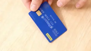 Una mano tiene una carta prepagata PostePay sopra un tavolo in legno chiaro