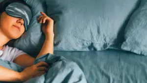 Persona che dorme a letto con lenzuola blu e mascherina per gli occhi