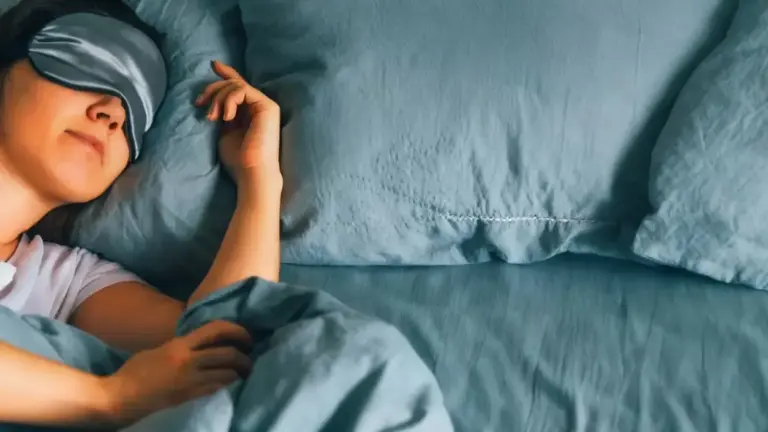 Persona che dorme a letto con lenzuola blu e mascherina per gli occhi