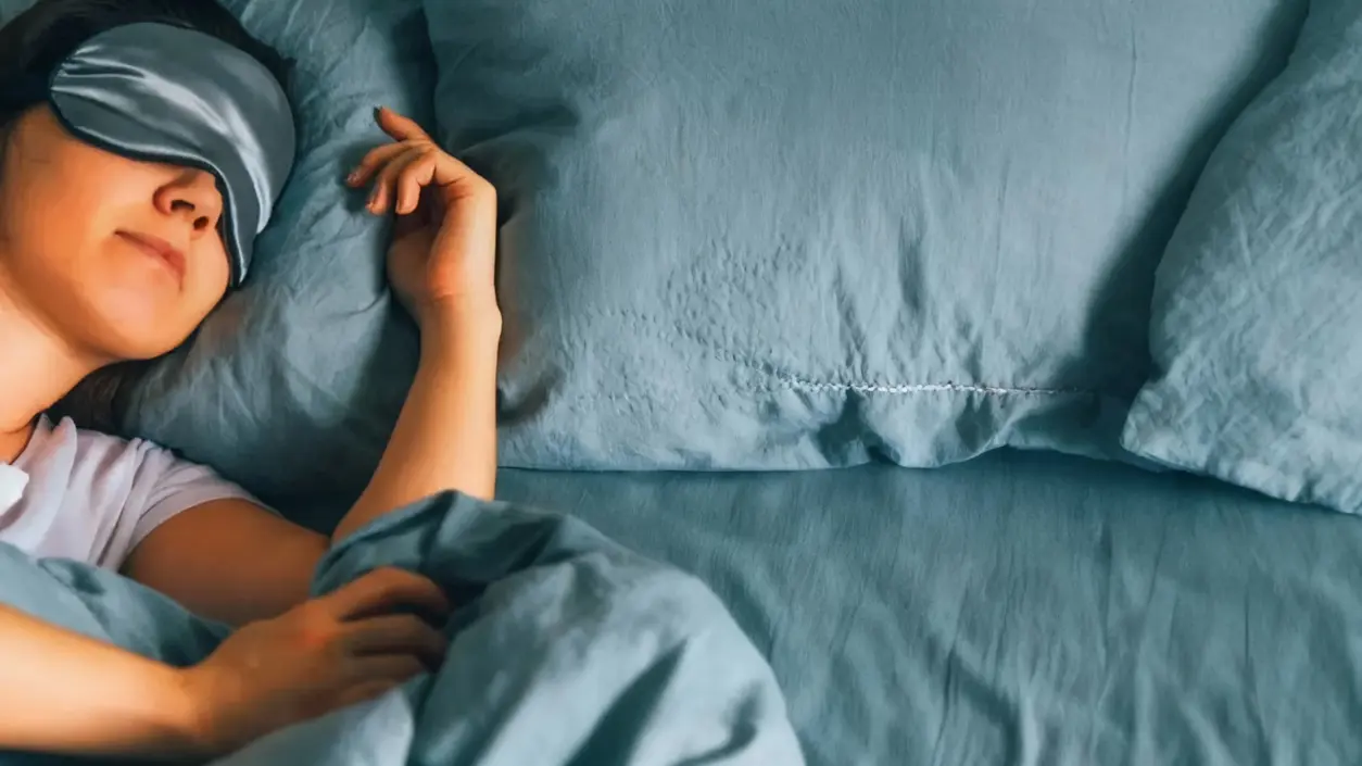 Persona che dorme a letto con lenzuola blu e mascherina per gli occhi