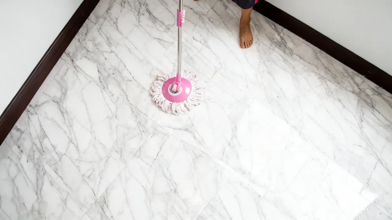 Una persona pulisce un pavimento in marmo con un mocio rosa