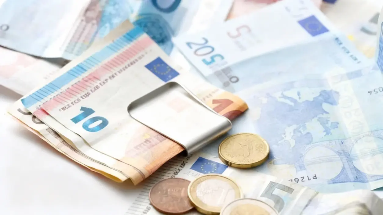 Banconote e monete in euro con fermasoldi su superficie chiara
