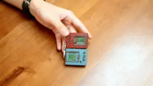 Una mano tiene due piccoli videogiochi portatili vintage su un tavolo di legno