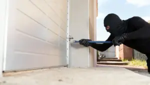 Persona incappucciata forza la serratura di una porta con un piede di porco